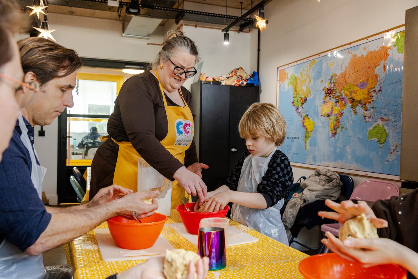 Group of people, including children, participating in a cooking activity with a world map in the background.