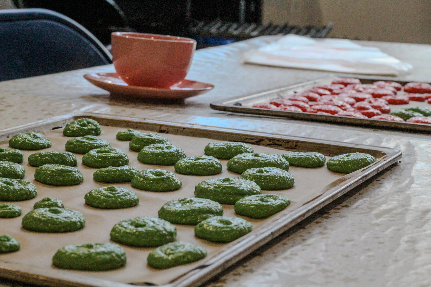 Green and Pink baked macaron bases sit on baking sheets, ready for assembly!