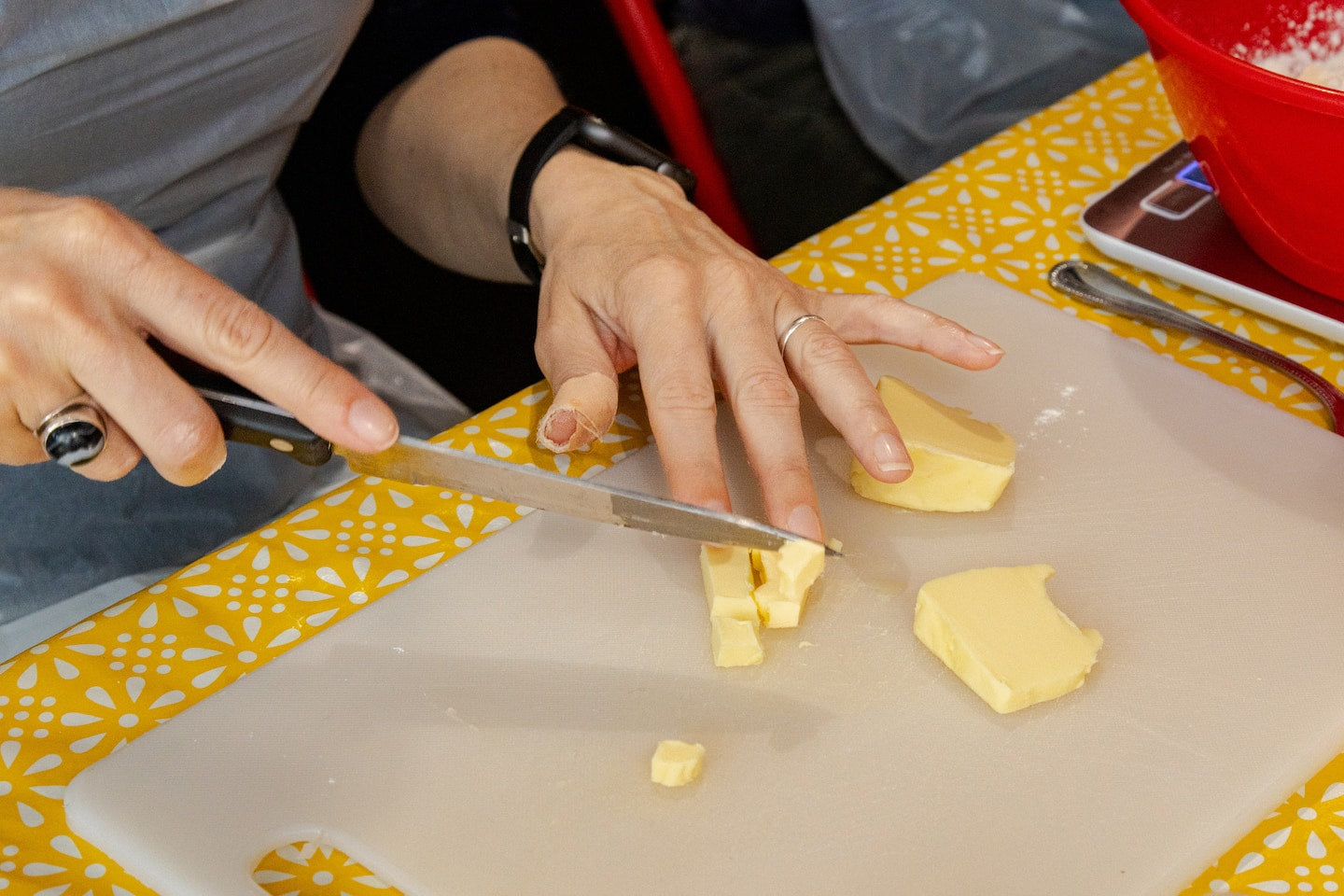 Person cutting butter on a cutting board with a yellow patterned tablecloth.