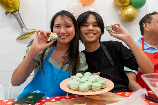 Two people, each holding up a macaron. The woman holds a plate filled with more.