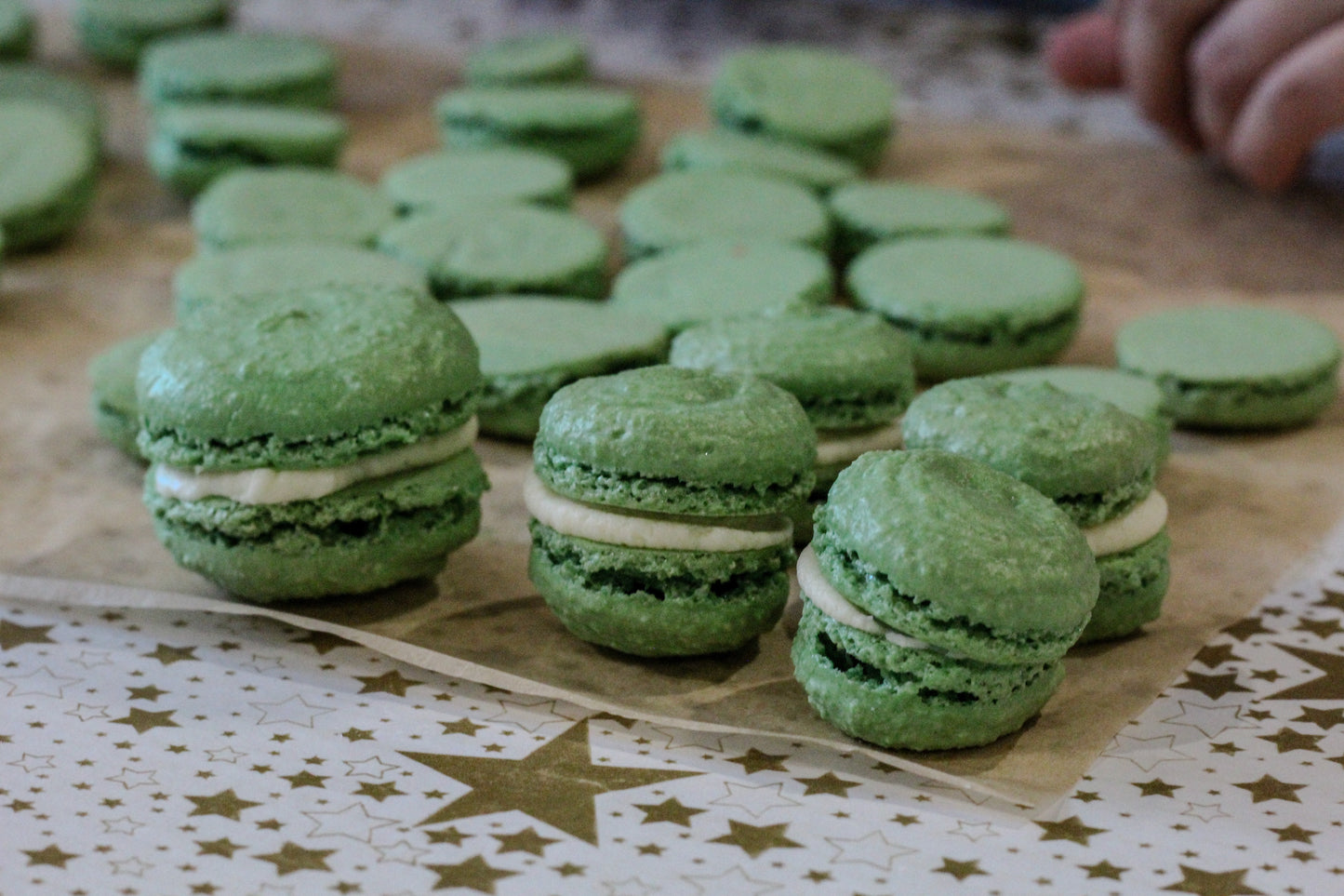 Green macarons with white filling on a baking sheet which sits on a star-patterned tablecloth