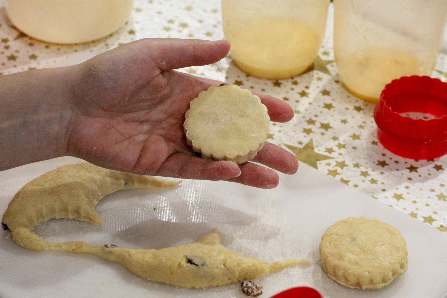 A hand presents a scone freshly cut using a cutter from a section of dough