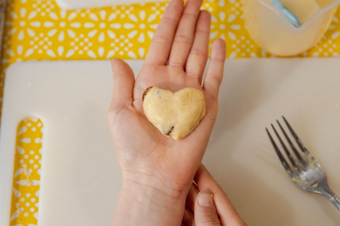 A hand holds a heart shape made from left-over dough.