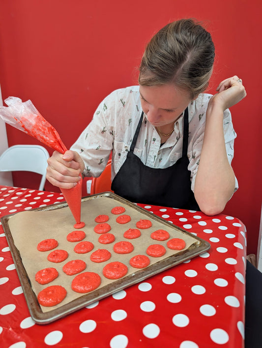 A woman pipes macaron bases onto a baking sheet