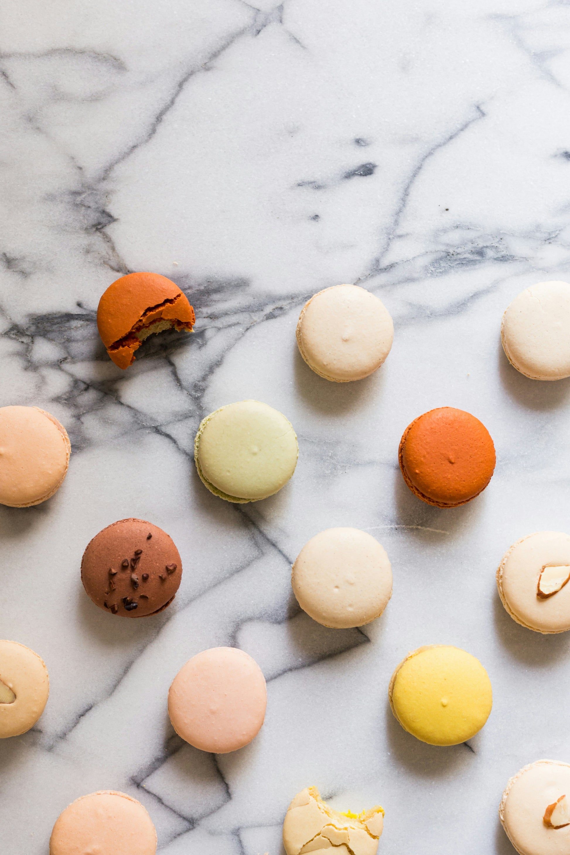 A variety of colorful macarons arranged on a marble surface.