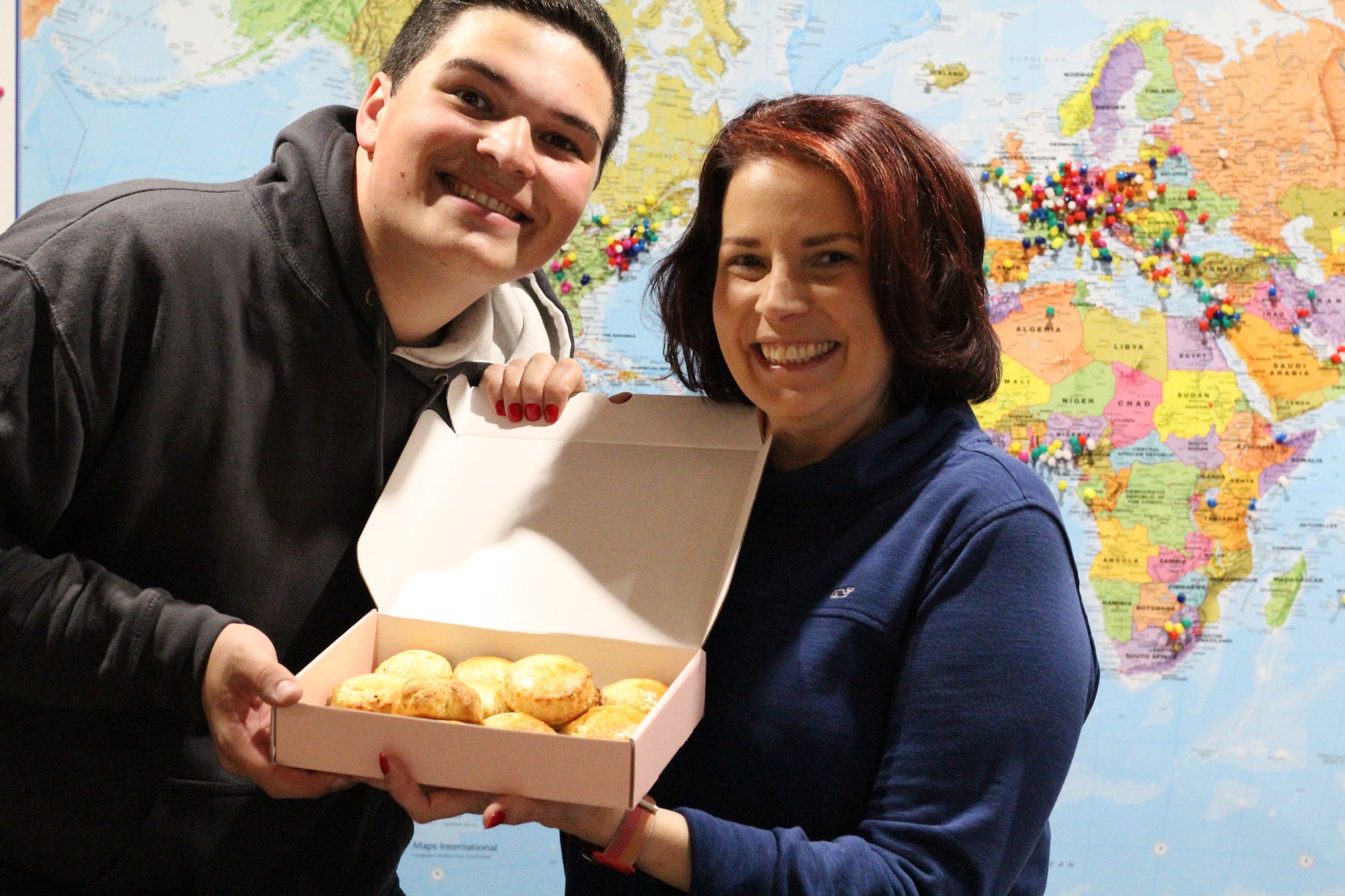A man and a woman show off their freshly-baked scones in front of a map of the world