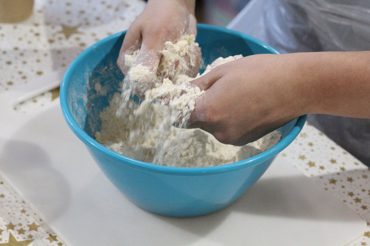 Person mixing dough ingredients in a blue bowl on a table