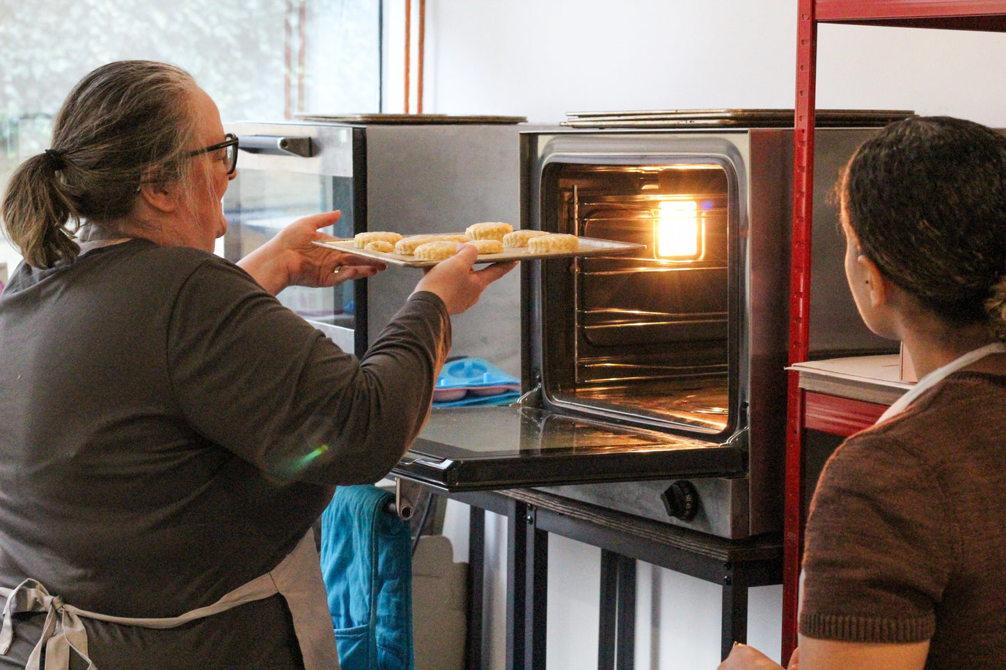 Course Leader Joanna places scones in the oven to bake while their maker looks on.