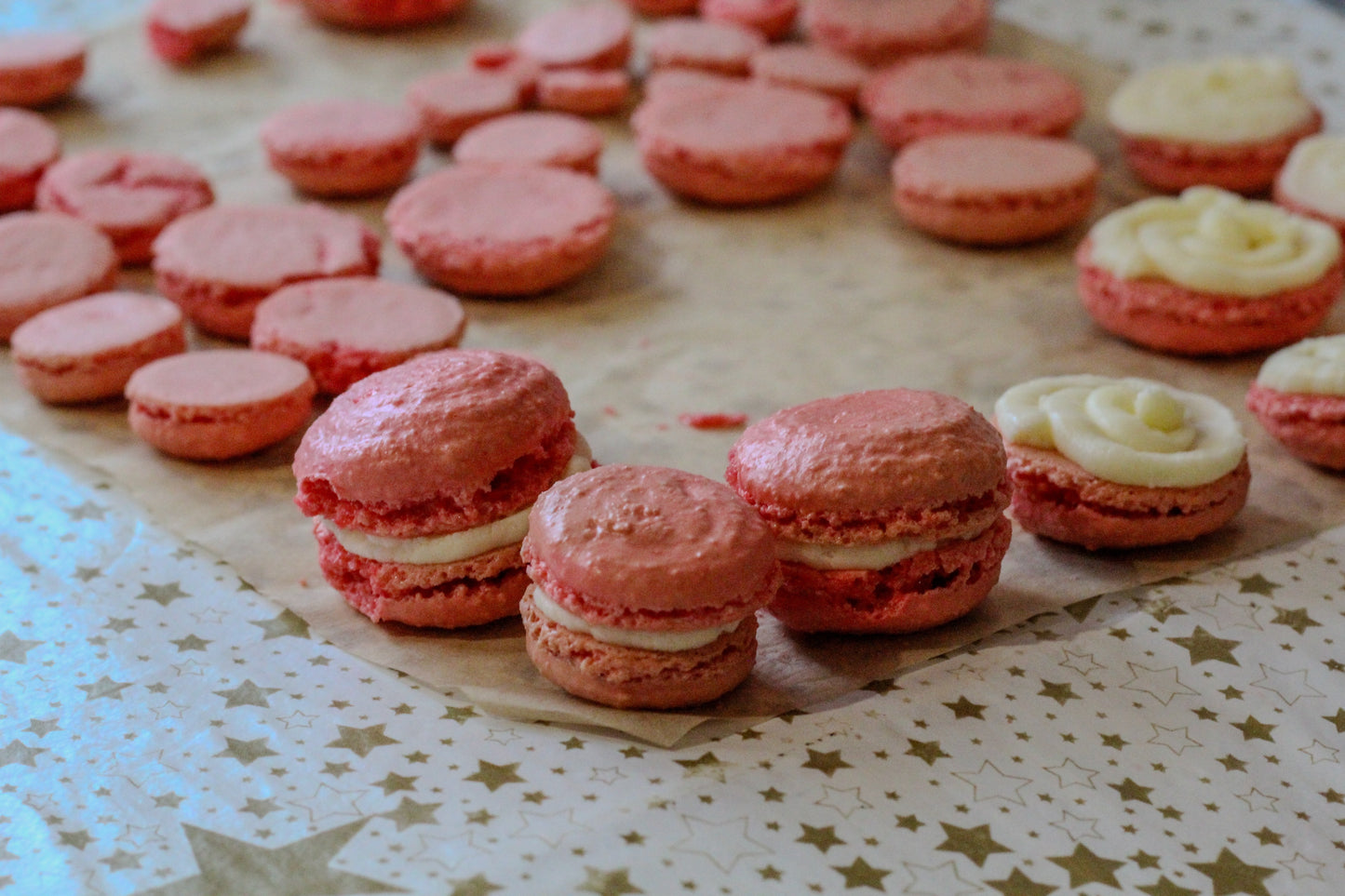 Pink macarons sit on a baking sheet upon a star-patterned tablecloth