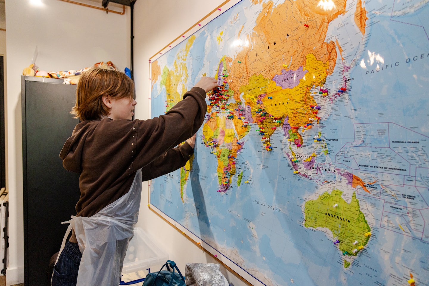 A child adds a pin to the world map to show how far they've come to visit the class
