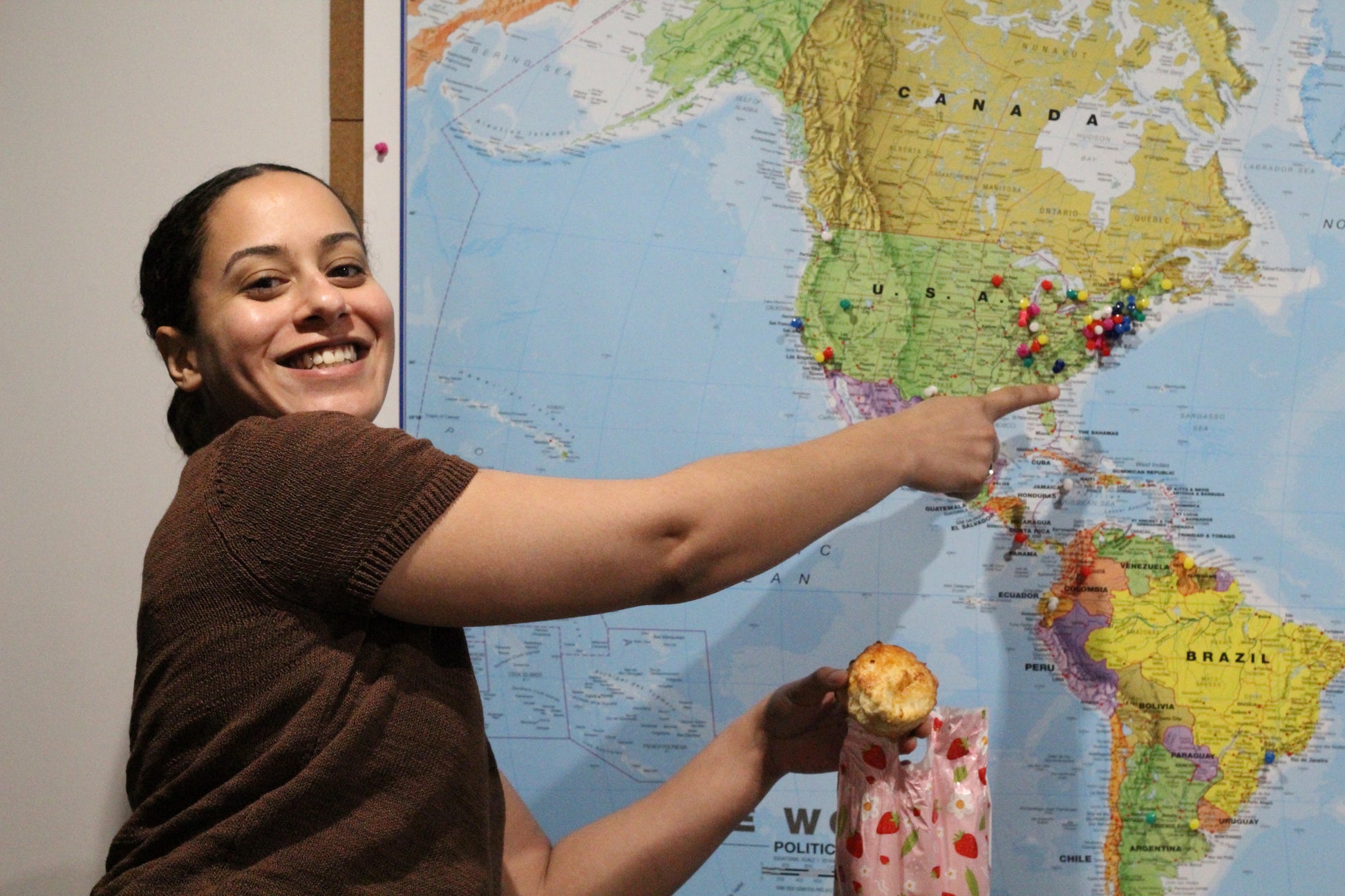 A happy customer points to where she comes from on a map of the world while holding a freshly-made scone.