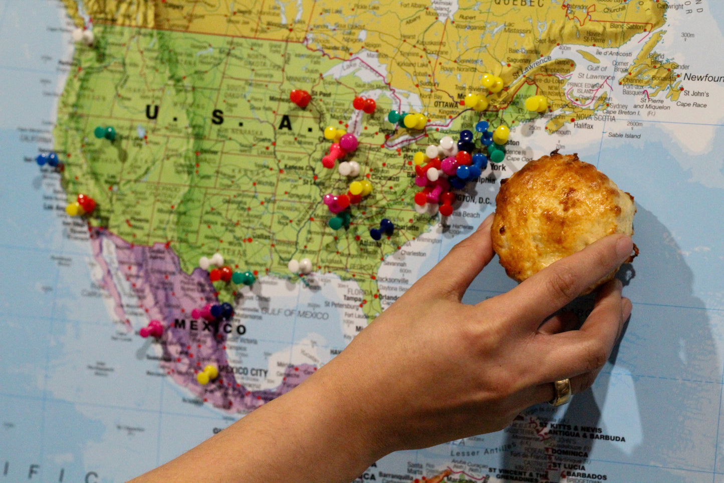 Hand holding a piece of food over a map of the USA with pins marking locations.