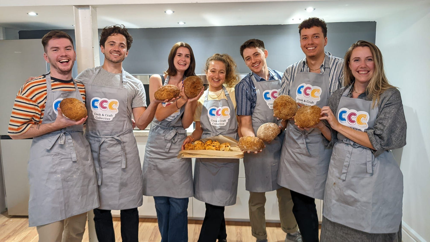 A group of young adults wearing grey Cook and Craft collective looking very happy with thier freshly baked bread after attending one of our bread making workshops