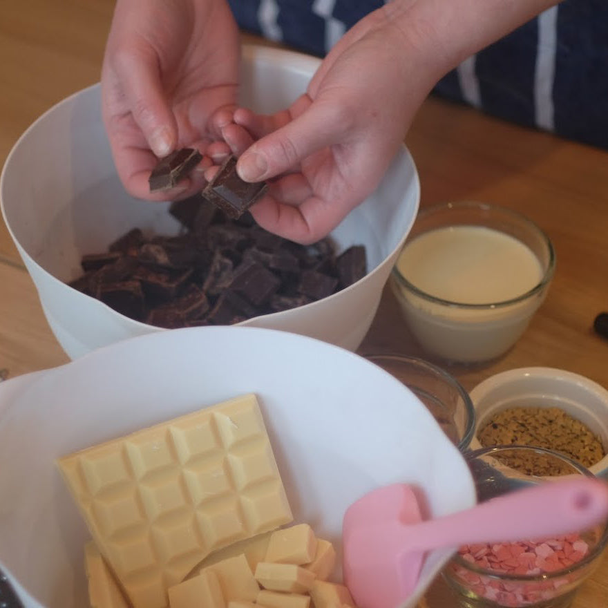 Make your own delicious chocolate truffles and use your favourite ingredients to create decadent treats from Cook and Craft Collective. image shows a person breaking up good quality chocolate into a bowl.